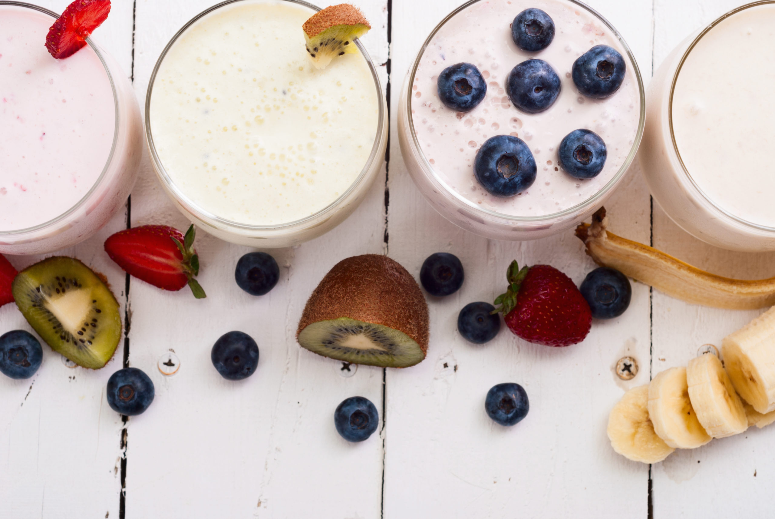 fruit smoothies met eiwit, blauwe bessen, kiwi, banaan en aardbeien op witte houten ondergrond over waarom je meer eiwitten zou moeten eten